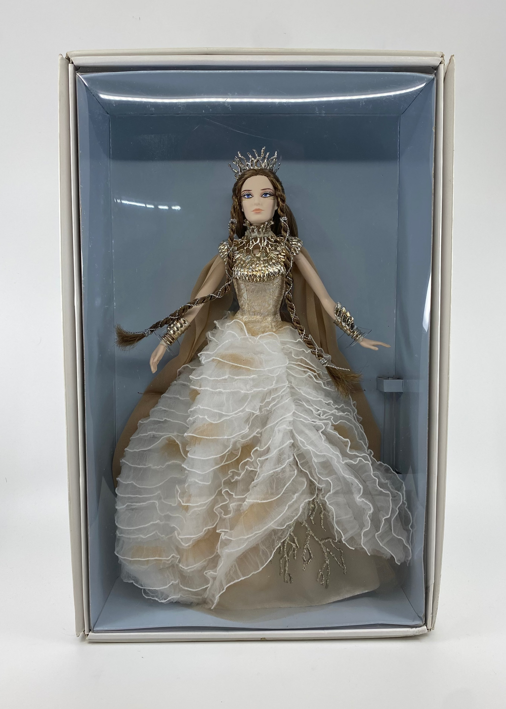 Doll in a decorative box with a white gown and crown on a light gray background