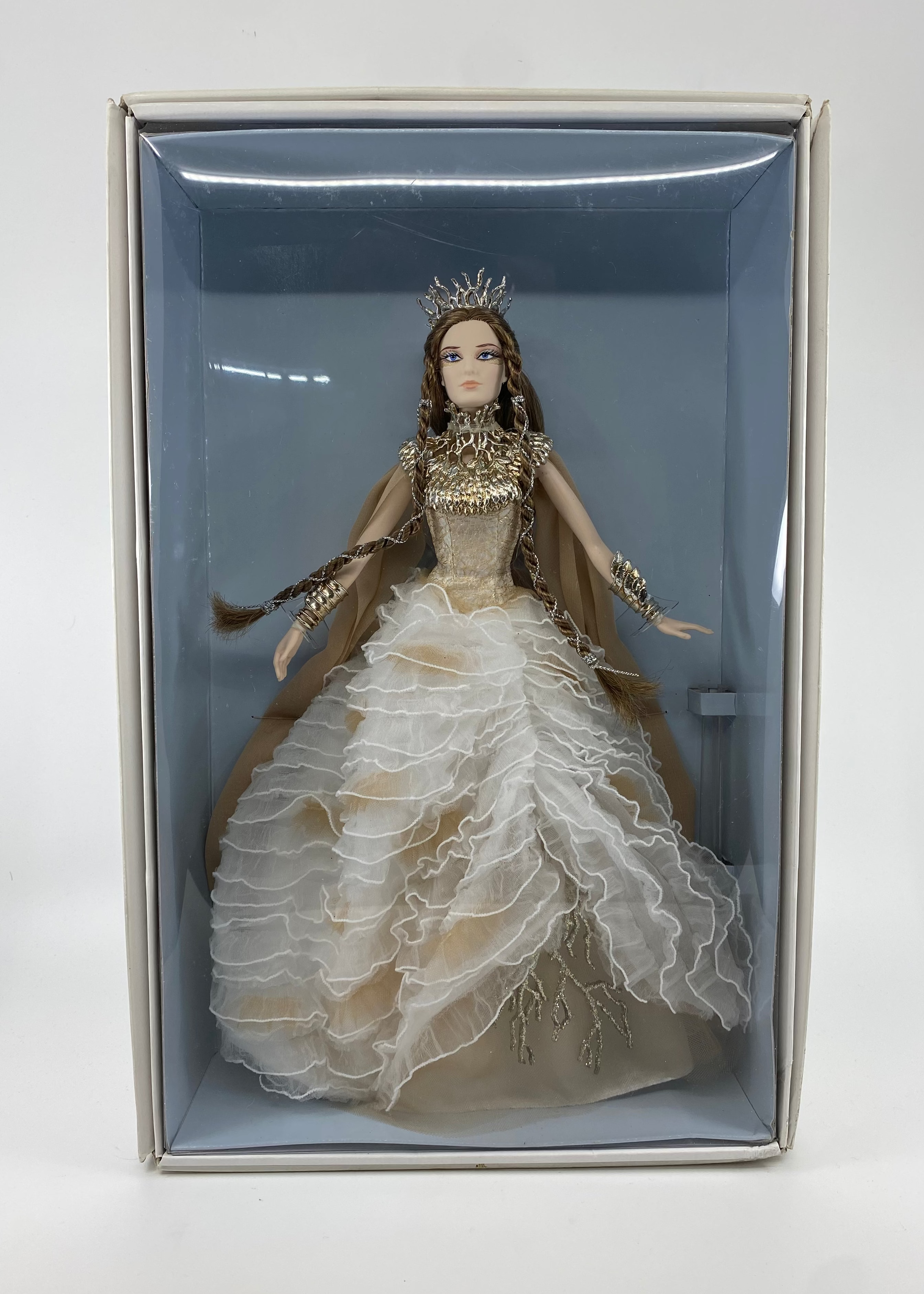 Doll in a decorative box with a white gown and crown on a light gray background