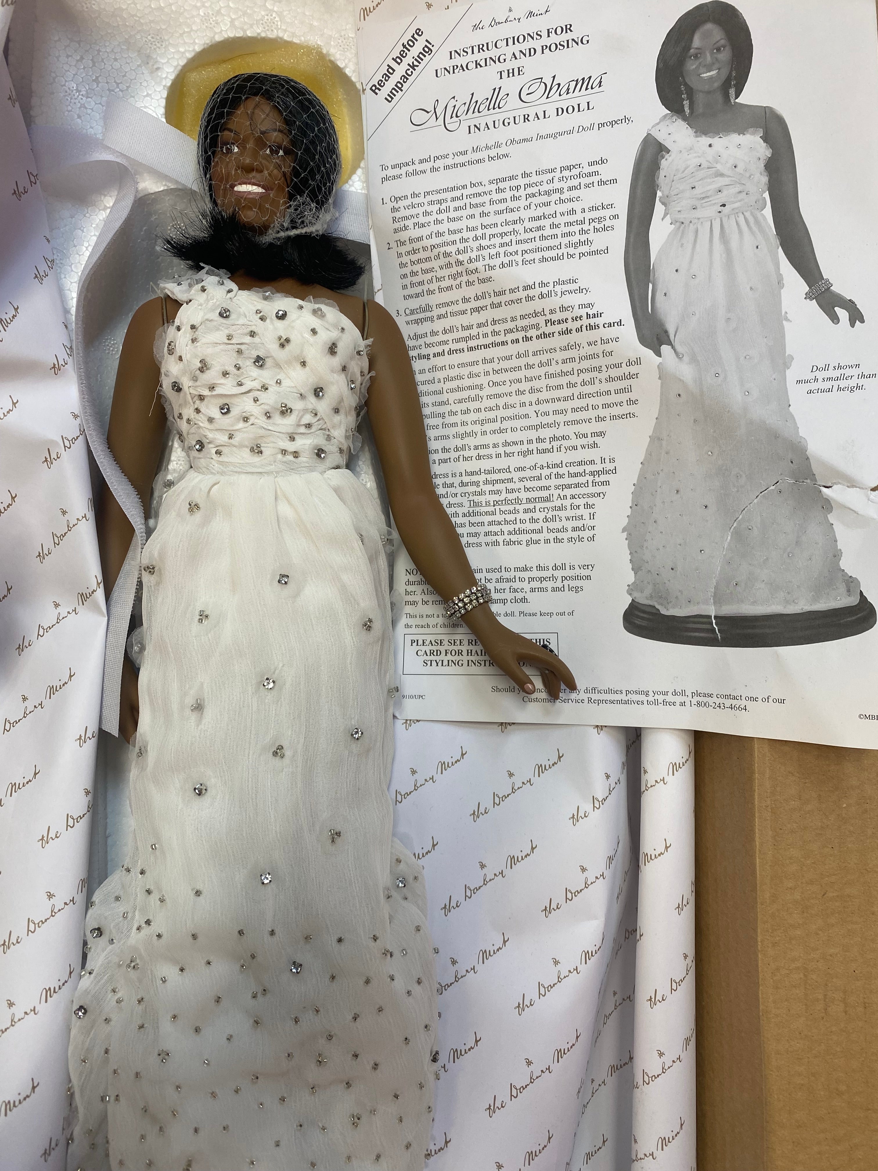Doll in a white dress with embellishments on a printed paper background