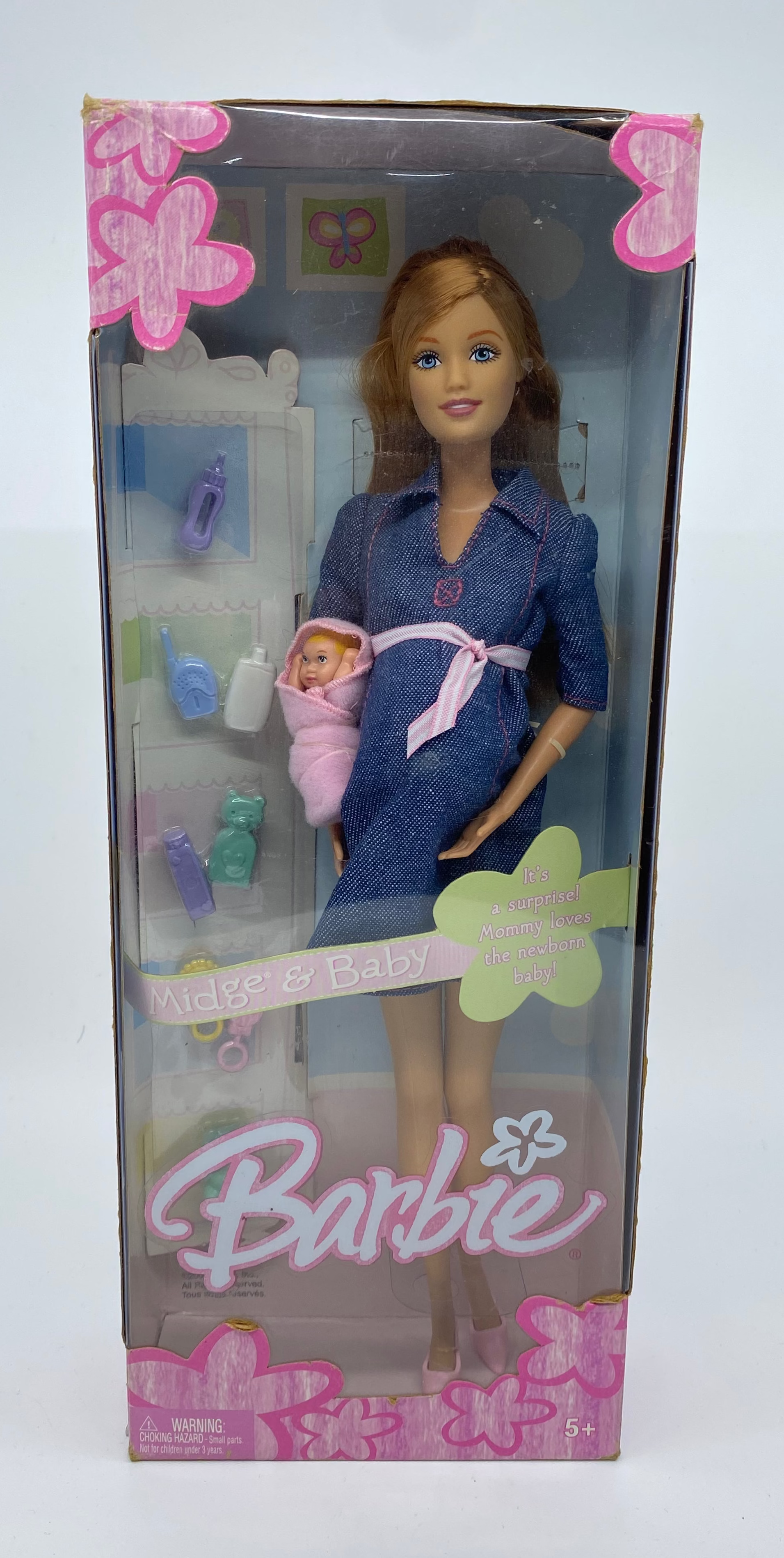 Barbie doll in a blue dress holding a baby in a packaging box on a white background