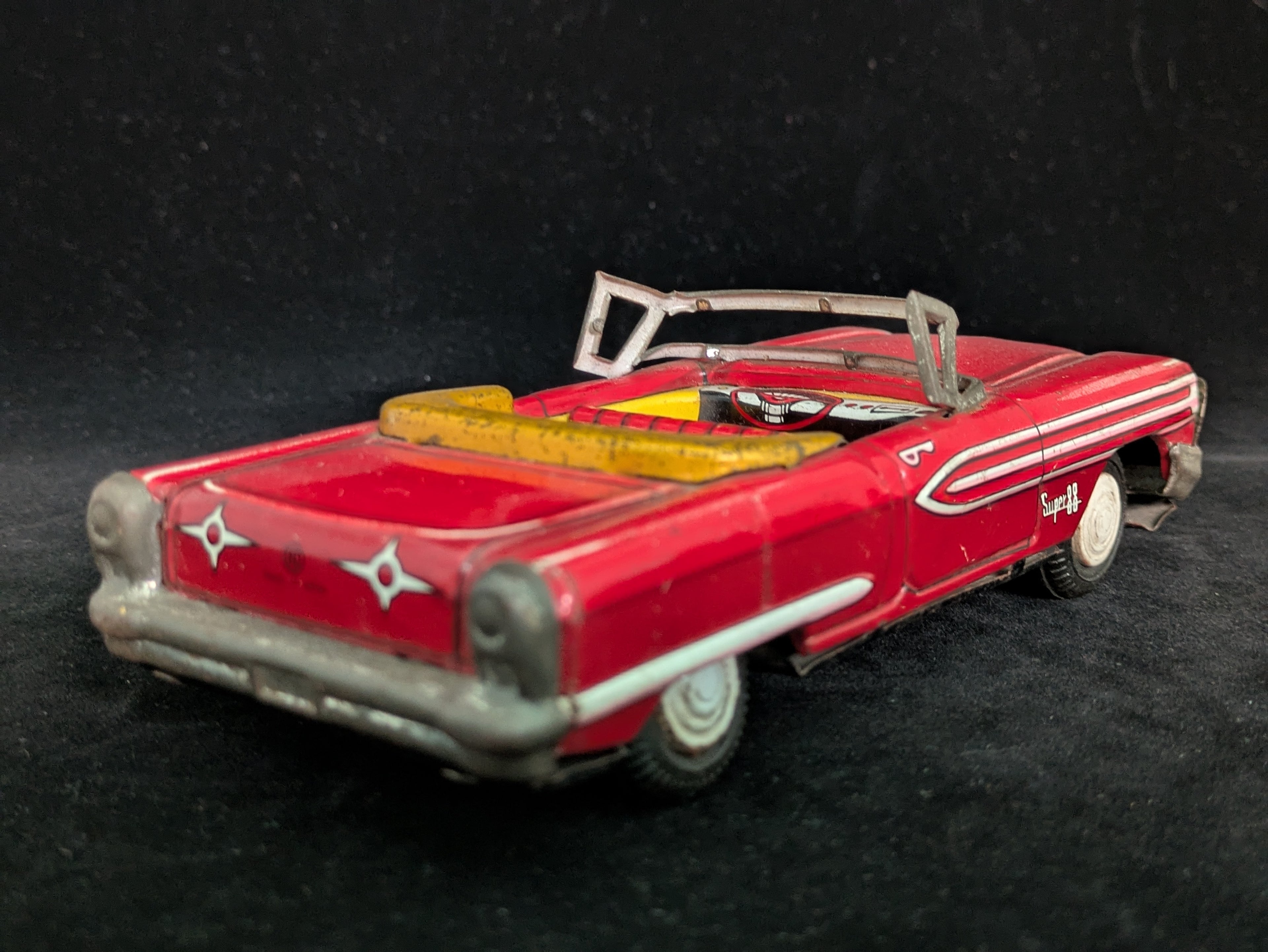 Vintage toy car with a red body and gray roof on a black background