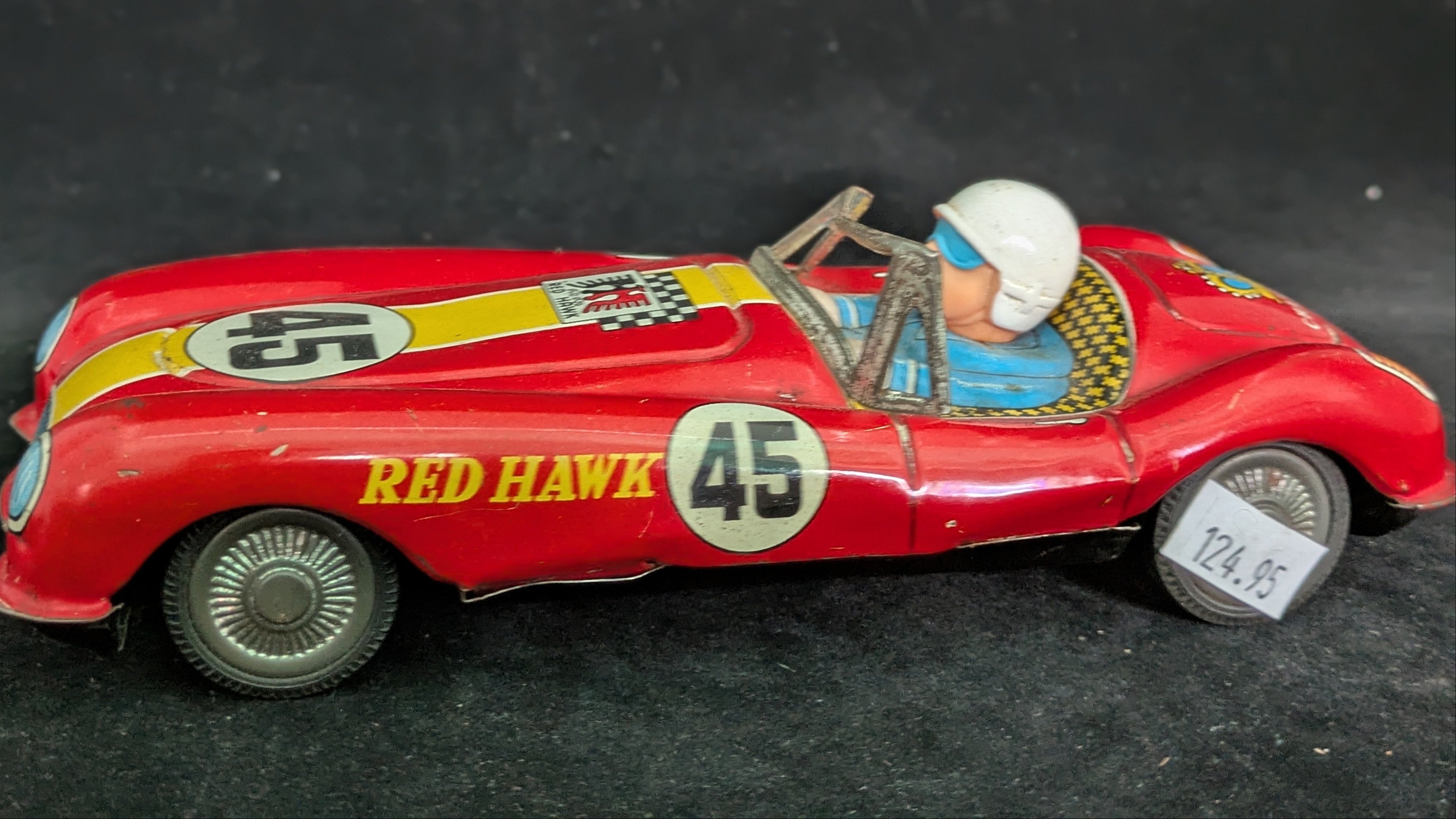 Vintage toy car model 'Red Hawk' with driver figure on a dark background