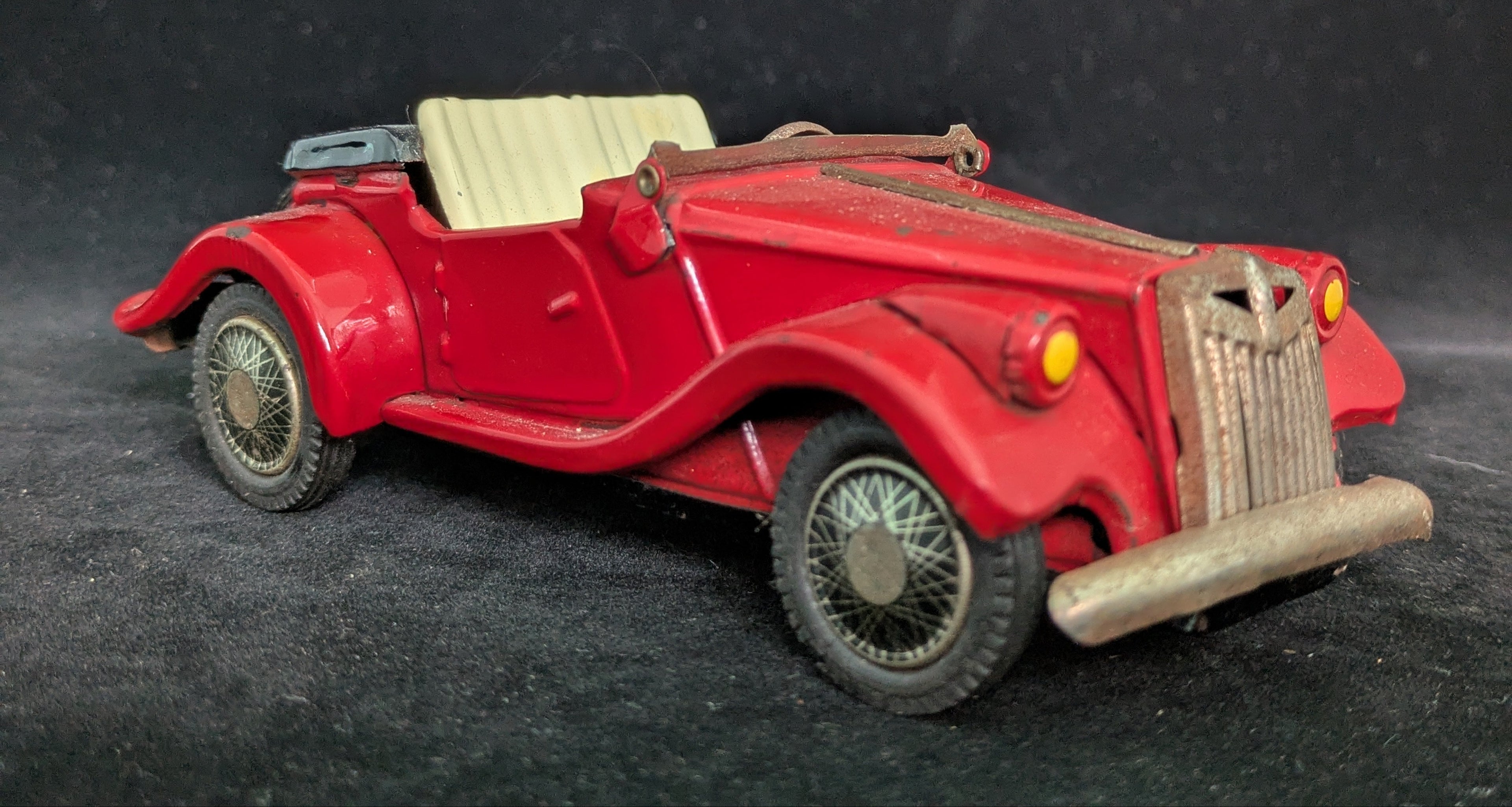 Red vintage toy car on a dark textured surface