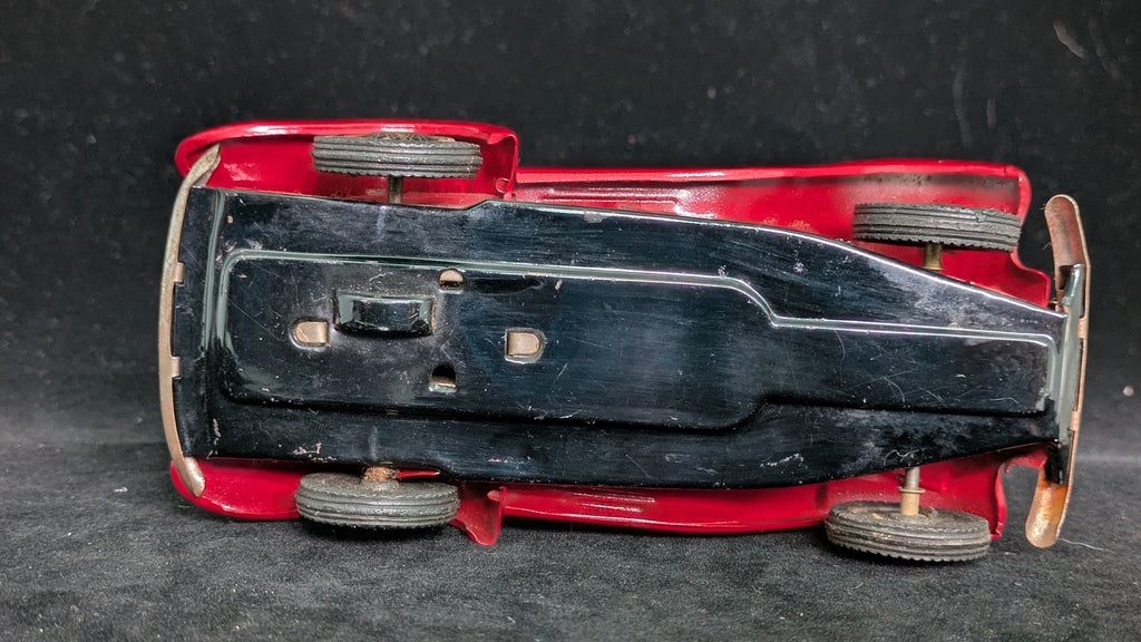Bottom view of a red toy car with black hood on a dark textured surface