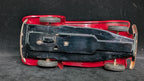 Bottom view of a red toy car with black hood on a dark textured surface