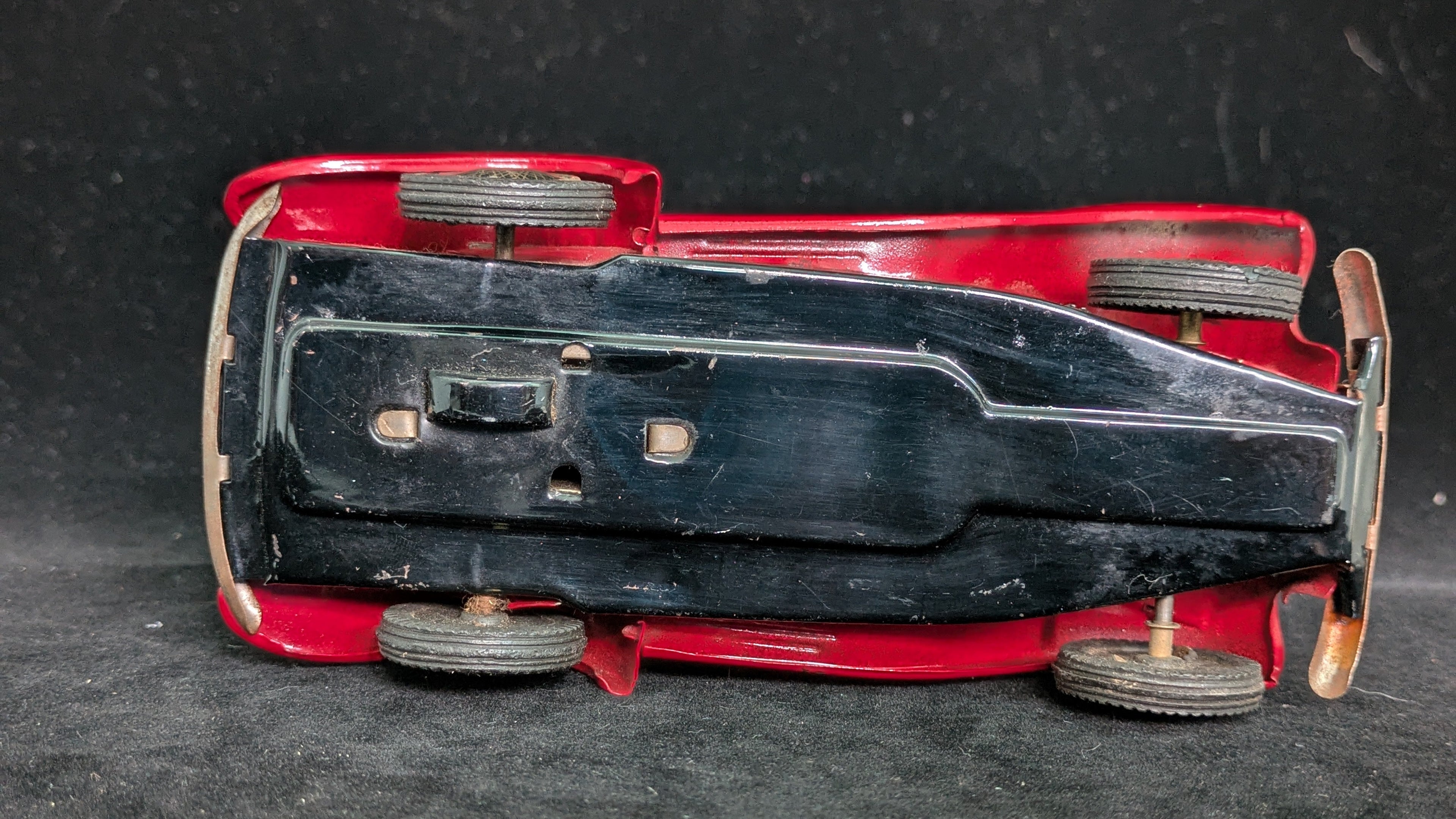 Bottom view of a red toy car with black hood on a dark textured surface