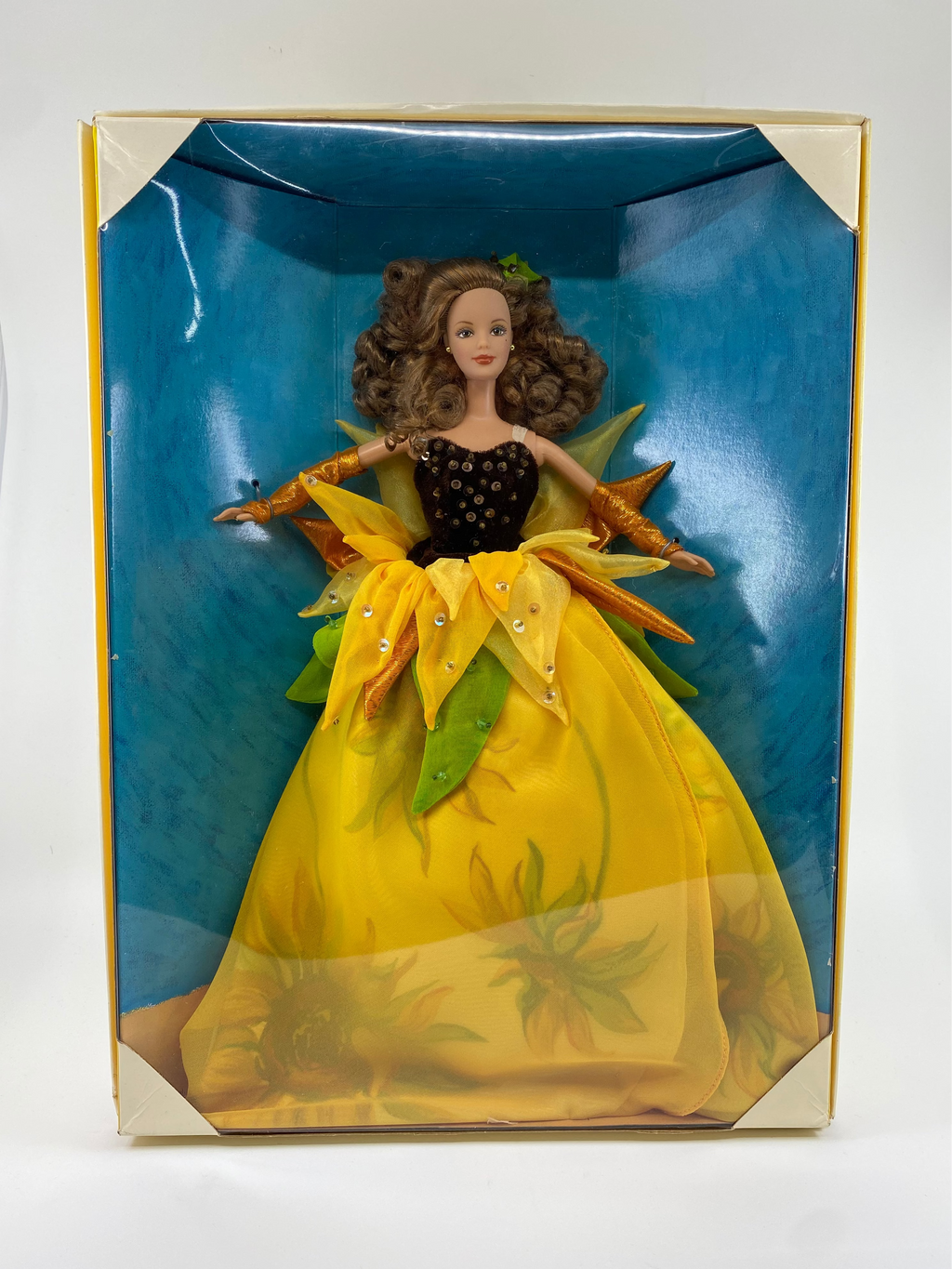 Doll in a yellow dress with green accents in a blue and gold box