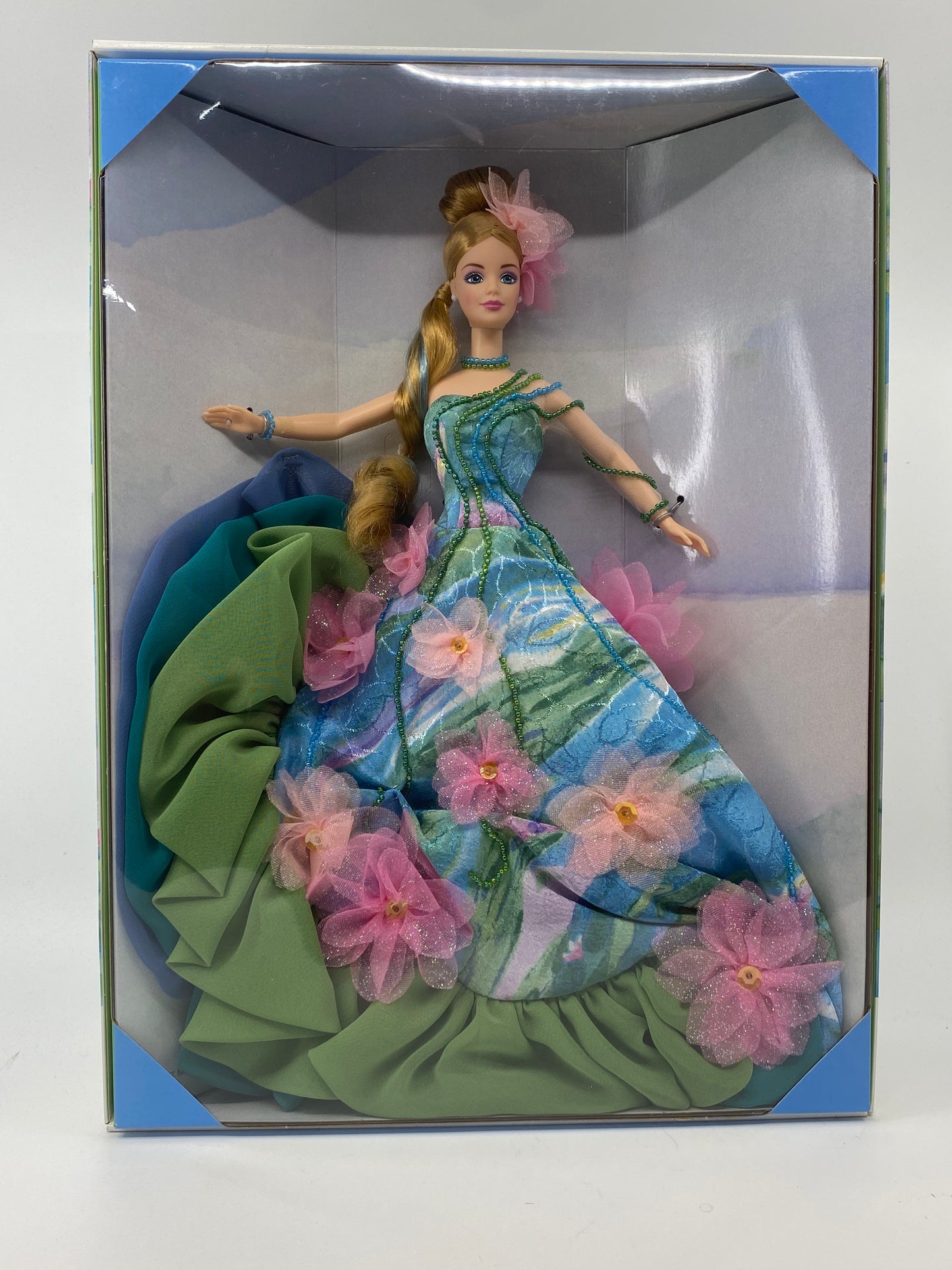 Doll in a floral dress with a green wrap, in a box on a white background