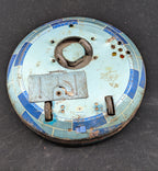 Round metallic component with blue and rust-colored finish on a dark background